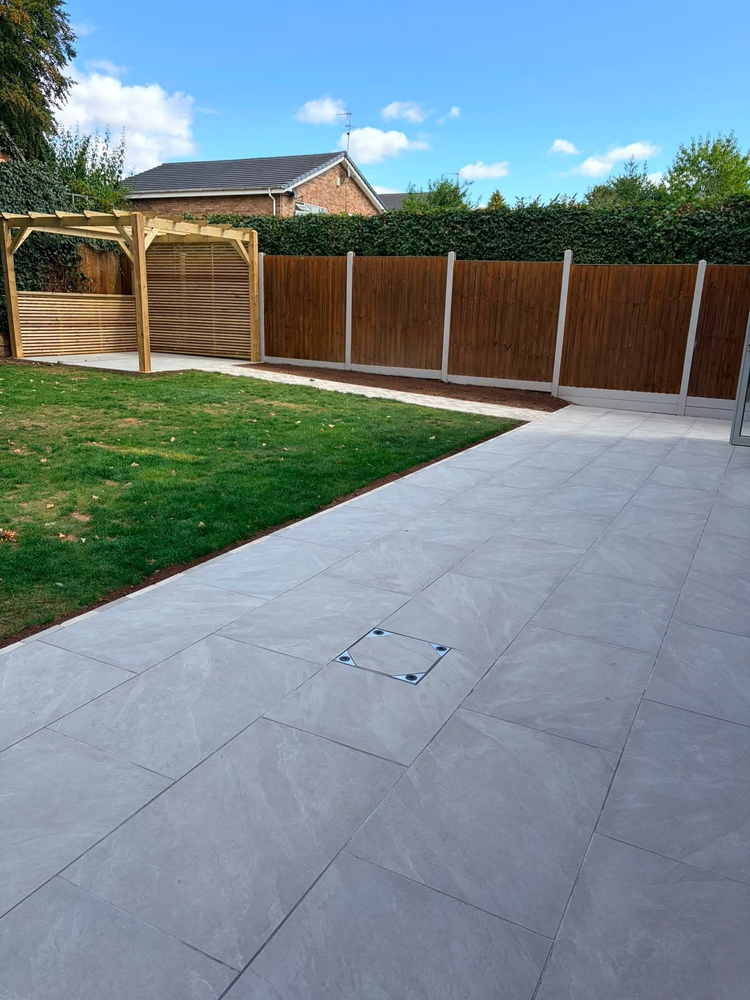 Large porcelain-style patio leading to a lawn and pergola